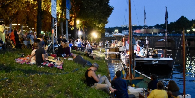 People lounging on the grass in front of the the theatre ship Maria Helena while moored at the bank of the river Saar