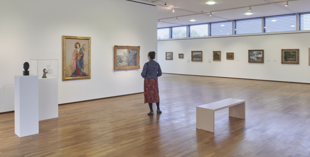 Visiteur à l'intérieur de la Moderne Galerie, œuvres d'art sur les murs, présentation des objets exposés dans des colonnes et banc de repos
