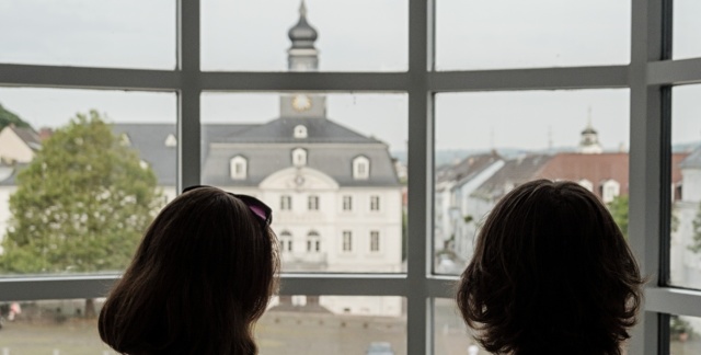 Zwei Personen blicken aus dem Glasbau des Saarbrücker Schlosses, über den Schlossplatz zum alten Rathaus