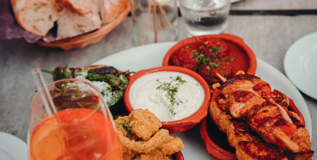 Ansicht von oben: Zwei Teller mit verschiedenen Tapas und Aufstrichen, sowie Brot, ein Glas Aperol Spritz und ein Glas Wasser