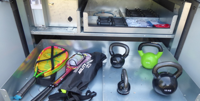 Sportbox drawer with four weights from four to 16 kilos, racket next to it. 