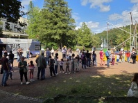 Eine Warteschlange steht für eine Hüpf-Attraktion an, im Hintergrund steht ein Lese-Bus
