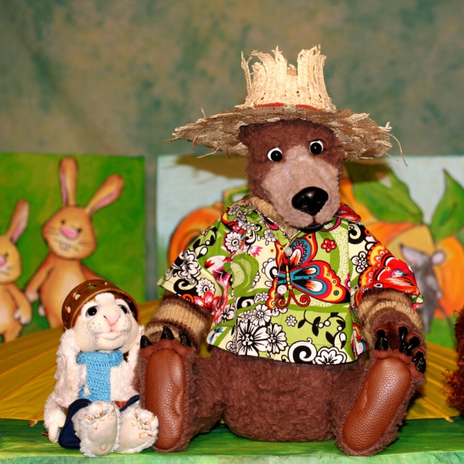 Eine Bärenpuppe mit Strohhut und buntem Hemd, eine kleine weiße Hasenpuppe und ein Stoffmurmeltier mit Hut sitzen nebeneinander.