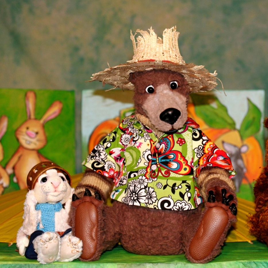 Eine Bärenpuppe mit Strohhut und buntem Hemd, eine kleine weiße Hasenpuppe und ein Stoffmurmeltier mit Hut sitzen nebeneinander.